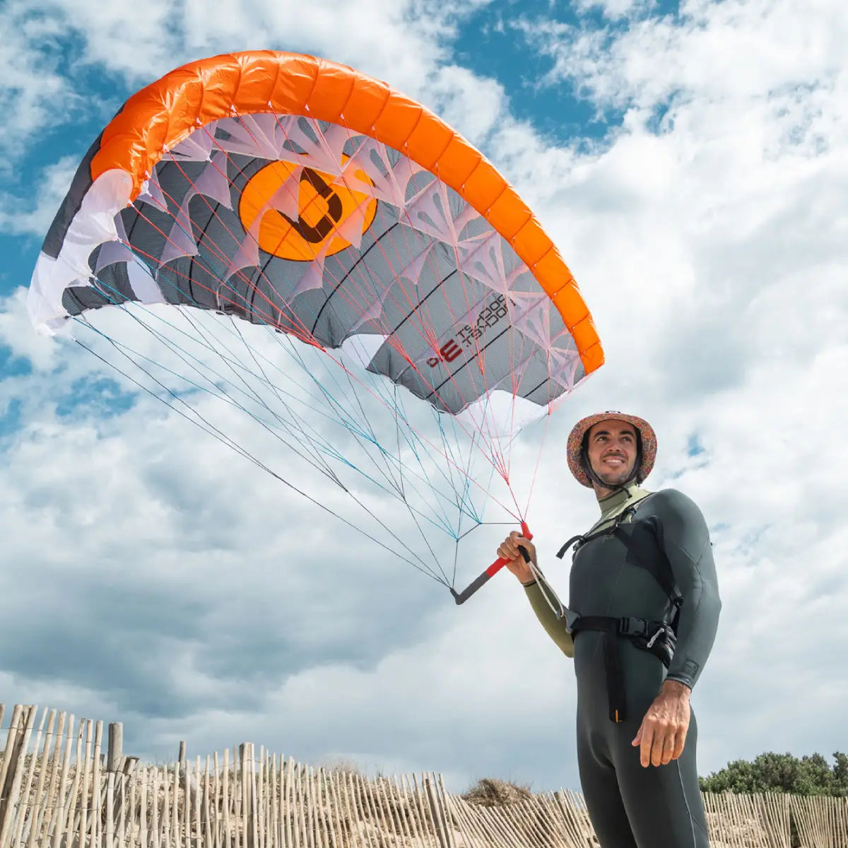 Parawing wingfoil surfare med nya Ozone Pocket Rocket V2 står på stranden med parawingen i luften